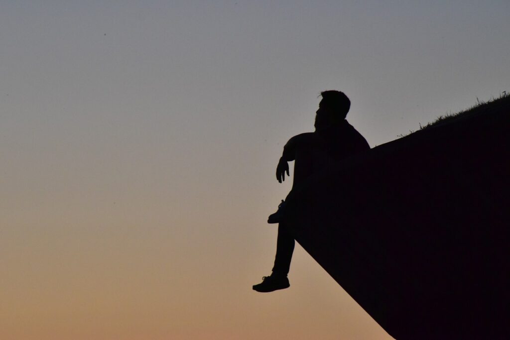 屋根の上で夕陽をぼんやり眺めている男性のシルエット